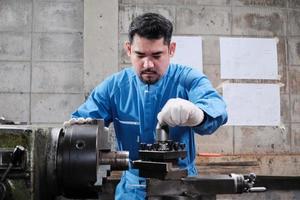 One professional Asian male industry engineer worker works in a safety uniform with metalwork precision tools, mechanical lathe machines, and spare parts workshop in the steel manufacturing factory. photo