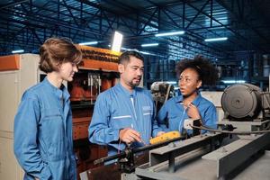 Los equipos multirraciales de ingenieros de la industria profesional con uniformes de seguridad trabajan inspeccionando la corriente de voltaje de las máquinas, comprobando y manteniendo en la fábrica de fabricación, ocupaciones de servicio del sistema eléctrico. foto