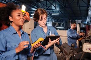 dos ingenieras profesionales con uniformes de seguridad trabajan inspeccionando la corriente de voltaje de las máquinas, comprobando y manteniendo en la fábrica de fabricación, ocupaciones de servicio del sistema eléctrico. foto