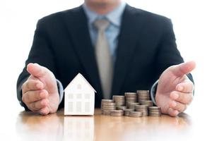Stack of increasing coins and house model with businessman crossing his arms photo