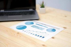 laptop and financial graph on white paper on working table photo