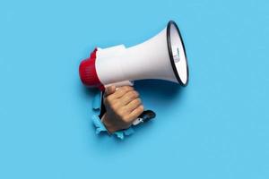 hand holds a megaphone blue background out of a torn hole in a paper background photo