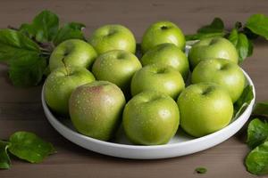 manzanas verdes maduras frescas y hojas de manzano en placa de cerámica blanca foto