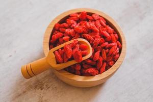 Dried Chinese wolfberries or Goji berry chinese herb or Matrimony vine in the woodden scoop on wooden bowl isolated on wooden background.  Selected focus. photo