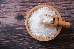 Flower of salt, is a salt that forms as a thin, delicate crust on the surface of seawater in the wooden scoop and wooden bowl on wooden background. Selective focus. photo