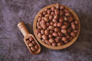 Raw Groundnuts in the wooden bowl on cement background. Top view. photo