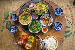 Vietnam family home cook set for four person cooked rice, vegetable soup and fried fishes, fried onions with chicken, cucumber slice, Vietnamese Traditional Meal in Country side. photo