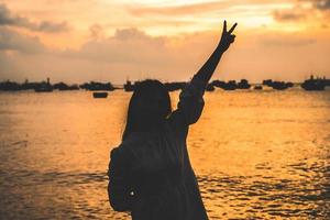 Focus back view happy Asian girl raises her hands up in front of beach at sunset. Travel concept. Concept welcoming, relaxing and enjoying. photo