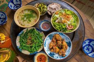 cocina casera de la familia vietnam preparada para cuatro personas arroz cocido, sopa de verduras y pescado frito, cebollas fritas con pollo, rodaja de pepino, comida tradicional vietnamita en el campo. foto
