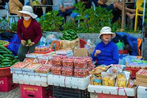 DA LAT - VIETNAM, APR 10 2022 Fruits and vegetables on a market in Da Lat Night Market. A female Vietnamese street vendor selling fresh strawberry photo