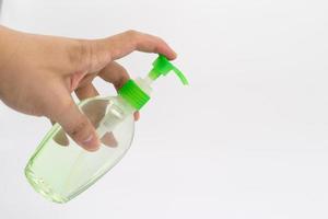 Asian mand hand holds a gel alcohol pump bottle and ready to pushes on it. It's an isolated object on the white clear screen in studio light. photo