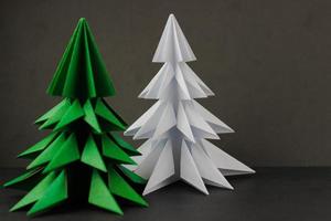 Two origami green and white christmas tree on black background. Focus on a white tree photo