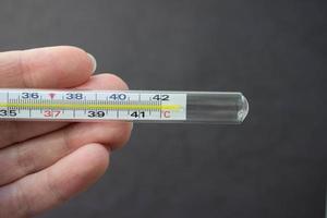 Mercury thermometer in hand on black background. Close up photo