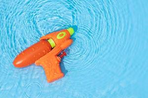 Water gun toy on blue water surface with rippled waves. Fun, leisure summertime background. Copy space photo