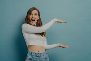 Shocked excited woman showing with hands big and large size measure symbol, isolated on blue photo