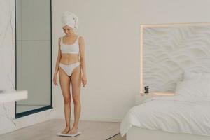 Attractive slim young girl standing on scales in bedroom photo