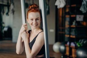 emocionada mujer pelirroja disfrutando del yoga aéreo en el estudio de fitness foto