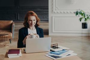 la mujer pelirroja contenta tiene trabajo a distancia, se comunica en video chat con colegas, discute ideas para proyectos, disfruta de la conferencia en línea usa una computadora portátil moderna y accesorios satisfechos con una conversación amistosa foto