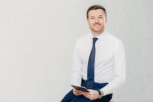 Intelligent lawyer in elegant clothes, holds digital tablet, spends free time in office, has pleasant smile on face, isolated over whte background with copy space for your advertising content photo