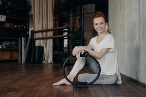 Smiling young sportive woman with pilates ring enjoying workout in fitness studio photo