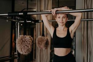 mujer joven en forma en ropa deportiva negra tomando un descanso en la máquina de pilates entre entrenamientos en el gimnasio foto