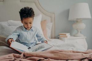 Cute afro american small boy trying to read children's book photo