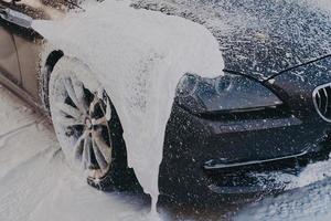 coche negro en espuma de jabón blanco en la estación de lavado foto