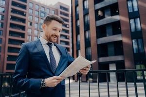 Exitoso y feliz economista masculino leyendo un artículo con noticias financieras en el periódico matutino foto