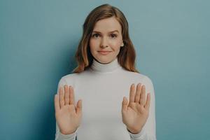 Attractive young focused woman showing stop gesture, saying no, isolated over blue studio background photo