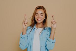 Young woman with crossed fingers on beige background photo