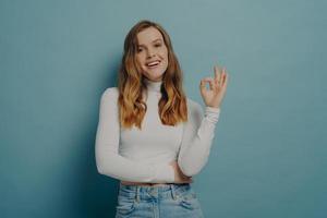 Cheerful excited young woman looking at camera with joyful smile while showing OK sign photo