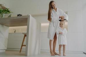 Loving mom brushing hair of cute little daughter after taking bath at home photo