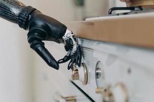 Carbon prosthetic hand of disabled is switching a stove on at kitchen. Routine of disabled person. photo