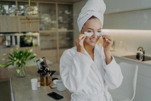 Happy woman in bathrobe and towel on head doing beauty or cosmetic procedures at home photo