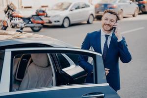 Confident executive talking on phone next to limousine photo