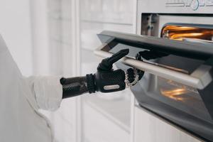 Robotic cyber hand of handicapped person is opening oven at kitchen and going to bake. photo