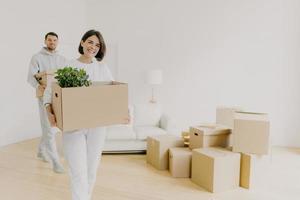 la mujer feliz y su esposo llevan cajas con pertenencias personales, están ocupados durante la reubicación en otro lugar para vivir, ingresan a un nuevo hogar, se mudan juntos en una casa grande, desempacan las cosas del hogar. foto