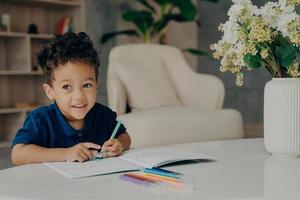 Cute afro american child painting in coloring book at home photo