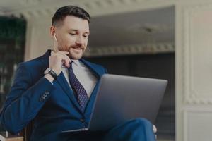 Young successful businessman having online meeting on laptop while sitting in office photo