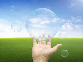 Hands trying to catch floating soap bubbles green green grass field and bright blue sky background photo