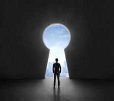 Businessman standing in front of bright big keyhole door, in a concrete wall with a view to the city photo