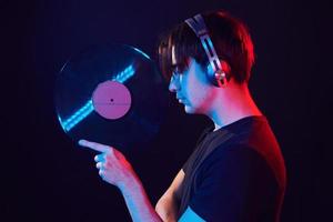 With vinyl record in hands. Man standing in the studio with neon light photo