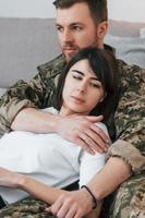 Sitting on the floor and ebracing the woman. Soldier in uniform is at home with his wife photo