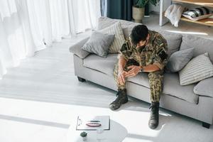 Bad mood. Post traumatic stress disorder. Soldier in uniform sitting indoors photo
