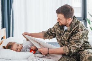 Peace and quiet. Soldier in uniform is at home with his little daughter photo