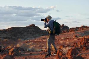 Using camera. Male tourist in casual clothes is in the deserts of Africa, Namibia photo