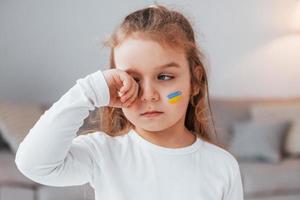 Innocent child is crying. Portrait of little girl with Ukrainian flag make up on the face photo