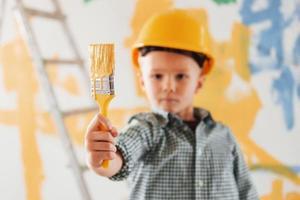 Blue and yellow colors behind. Conception of Ukraine and peace. Little boy painting walls in the domestic room photo