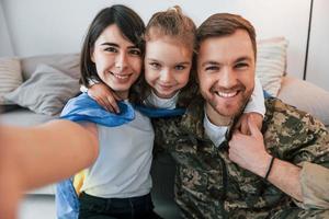 Making selfie. Soldier in uniform is at home with his wife and daughter photo