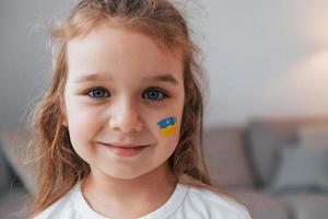 Smiling and having good mood. Portrait of little girl with Ukrainian flag make up on the face photo